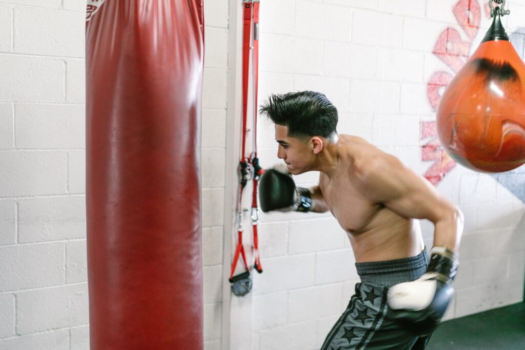 man throwing a hook on the punching bag, boxer hitting heavybag while wearing boxing gloves