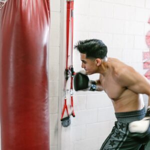 man throwing a hook on the punching bag, boxer hitting heavybag while wearing boxing gloves