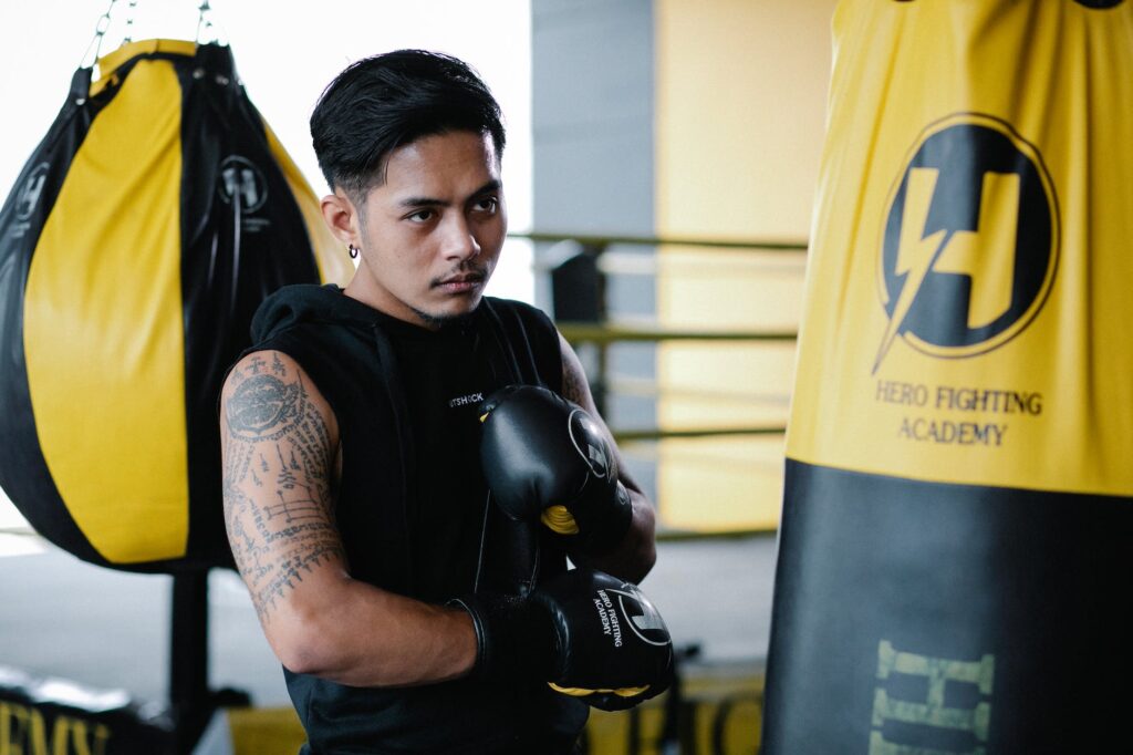 confident american male boxer standing near punching bag in gym