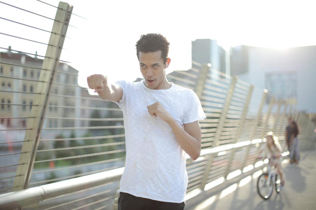 cheerful young ethnic sportsman listening to music and having fun pretending as boxer on street